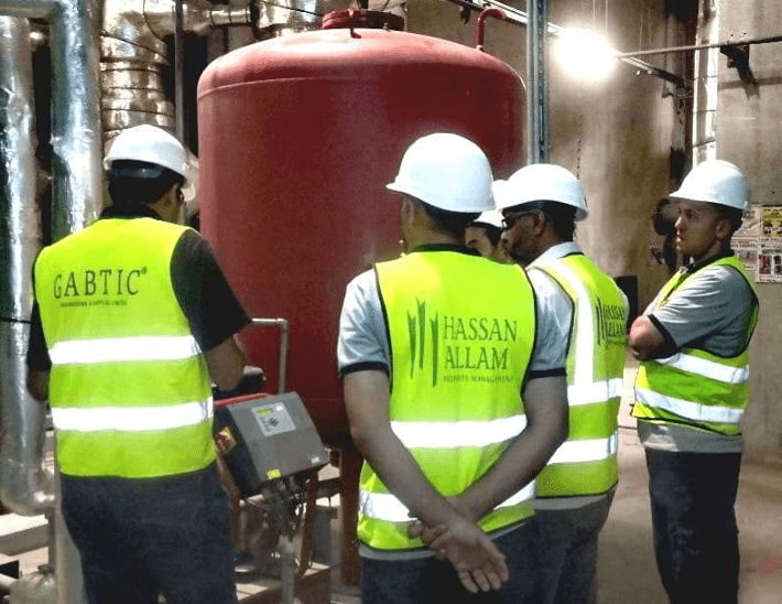GABTIC engineer briefing Hassan Allam property management staff beside an expansion tank in a plant room